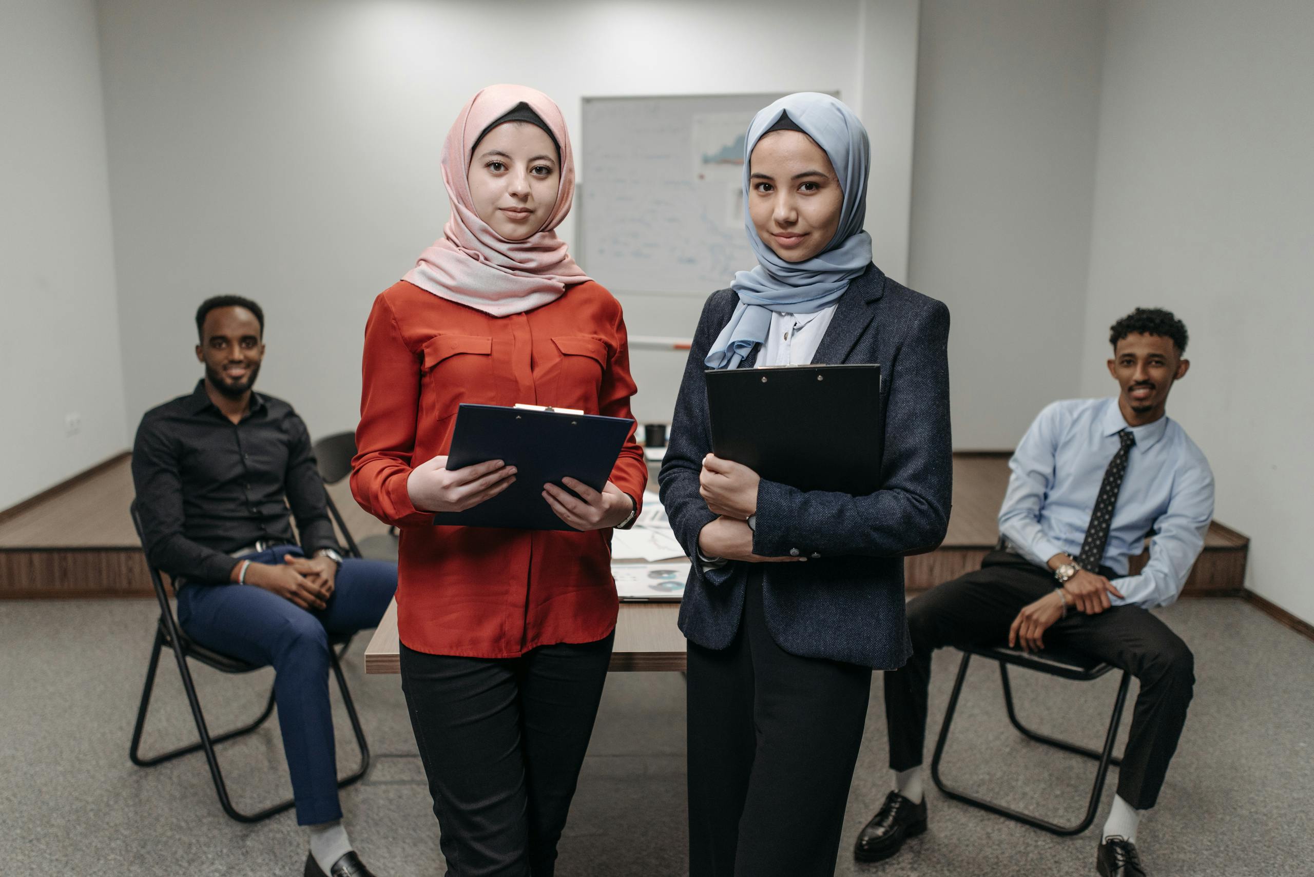 Two women in hijabs and two men having a business meeting in an office setting.